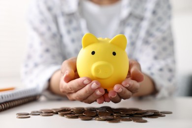 Woman with piggy bank and coins on white table indoors, closeup