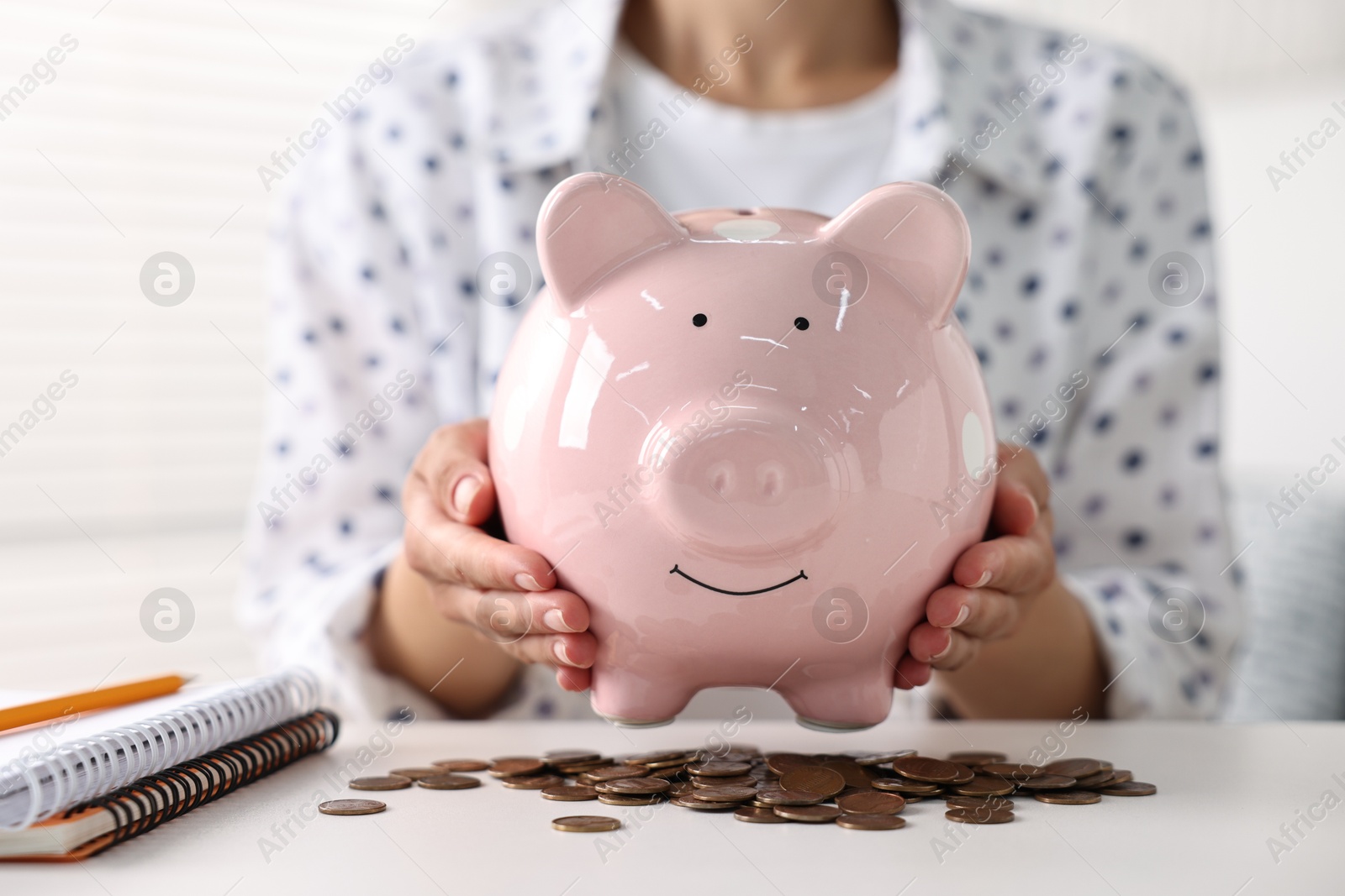 Photo of Woman with piggy bank and coins on white table indoors, closeup