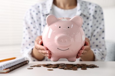 Woman with piggy bank and coins on white table indoors, closeup