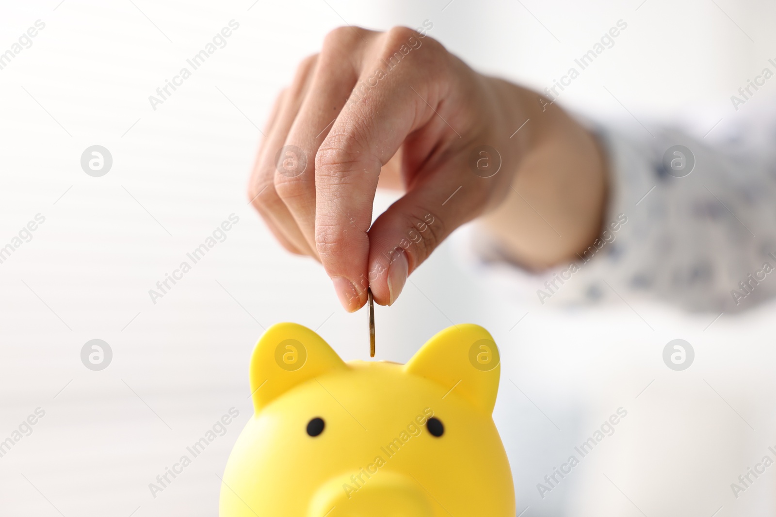 Photo of Woman putting coin into piggy bank indoors, closeup