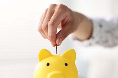 Woman putting coin into piggy bank indoors, closeup