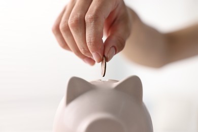 Woman putting coin into piggy bank indoors, closeup