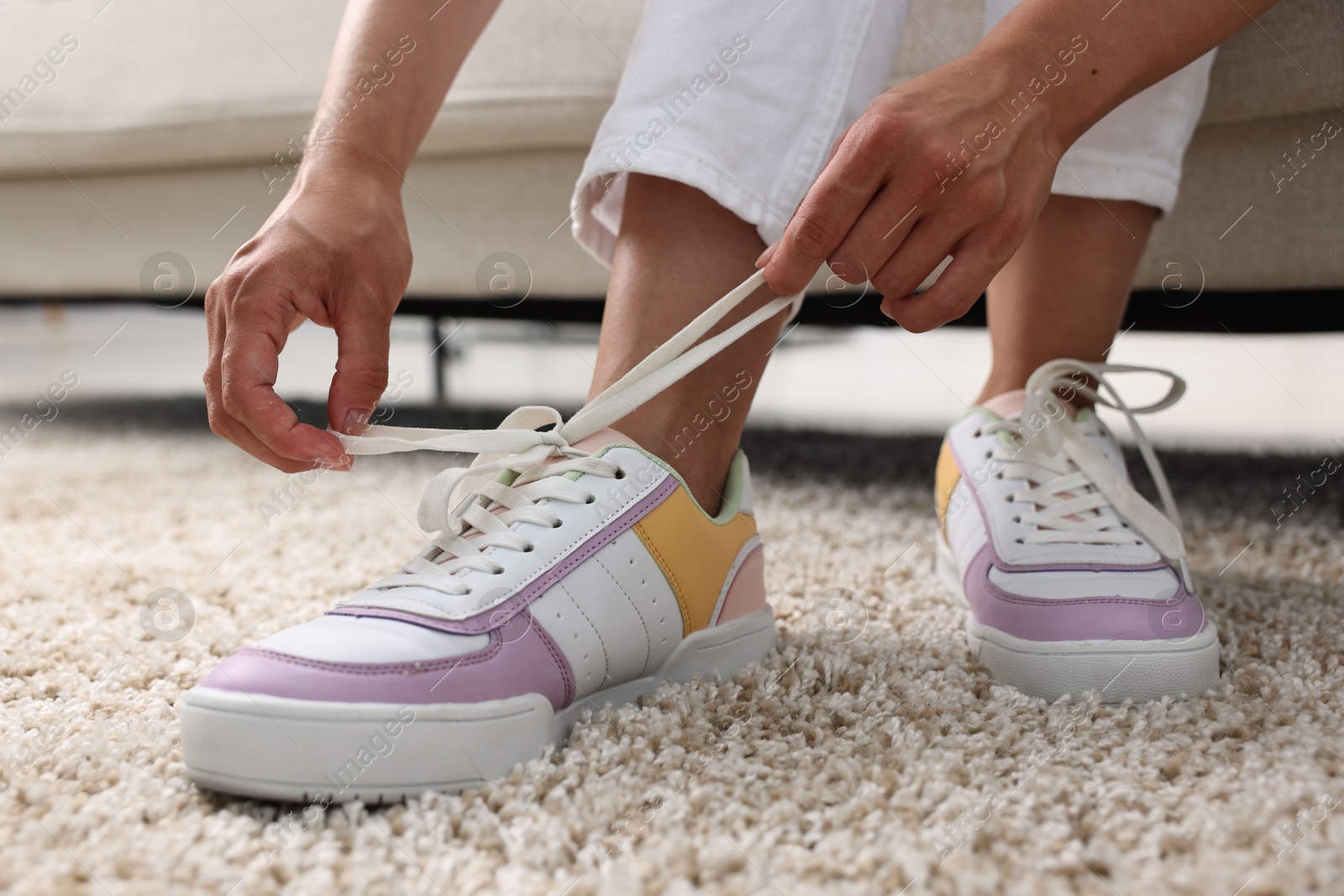 Photo of Woman tying shoelace of sneaker indoors, closeup