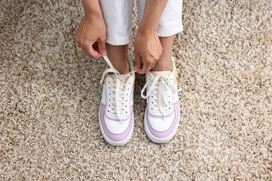 Photo of Woman tying shoelace of sneaker indoors, above view