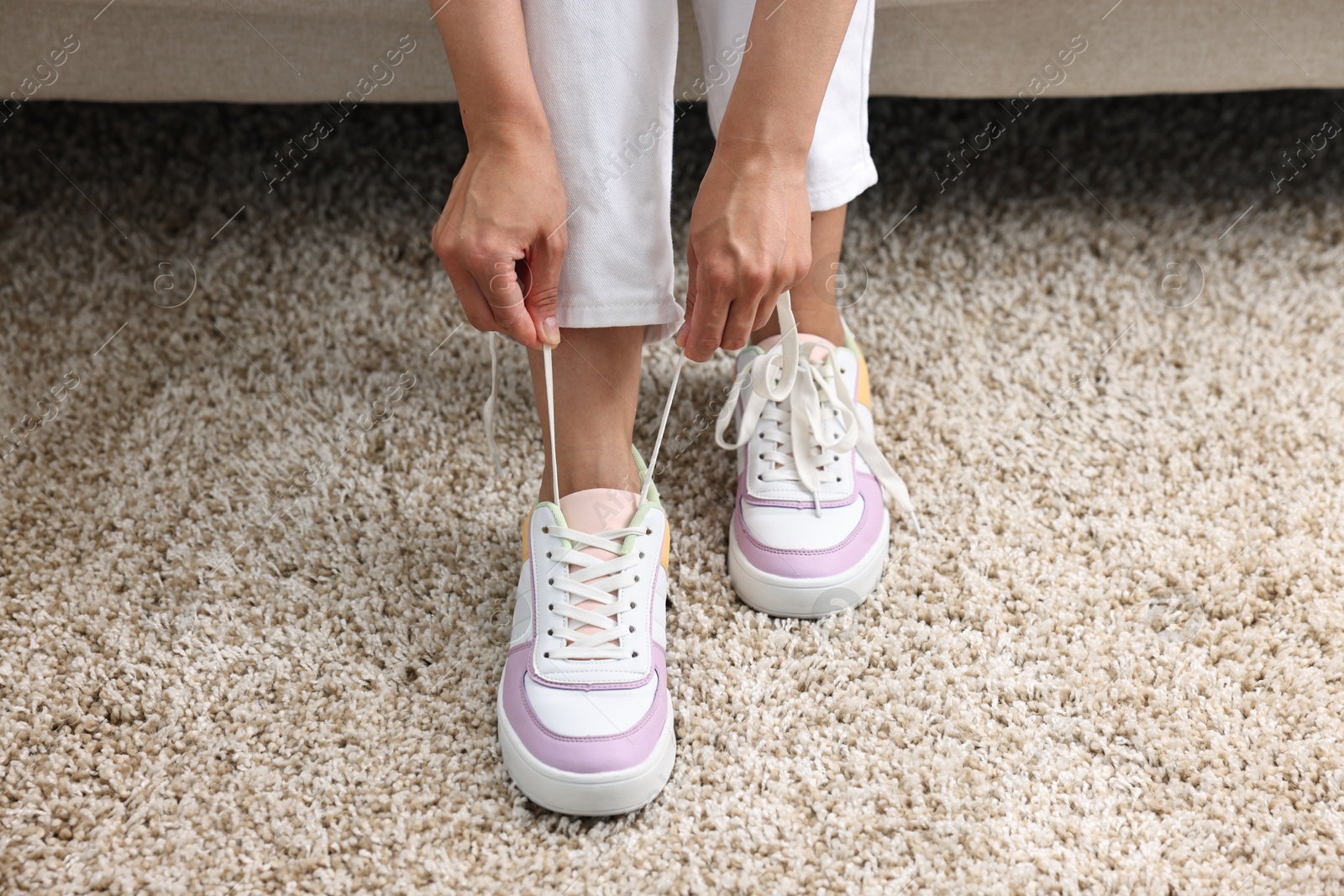 Photo of Woman tying shoelace of sneaker indoors, closeup