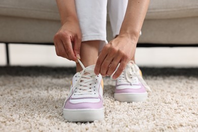 Woman tying shoelace of sneaker indoors, closeup