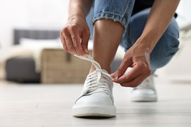 Photo of Woman tying shoelace of white sneaker indoors, closeup. Space for text