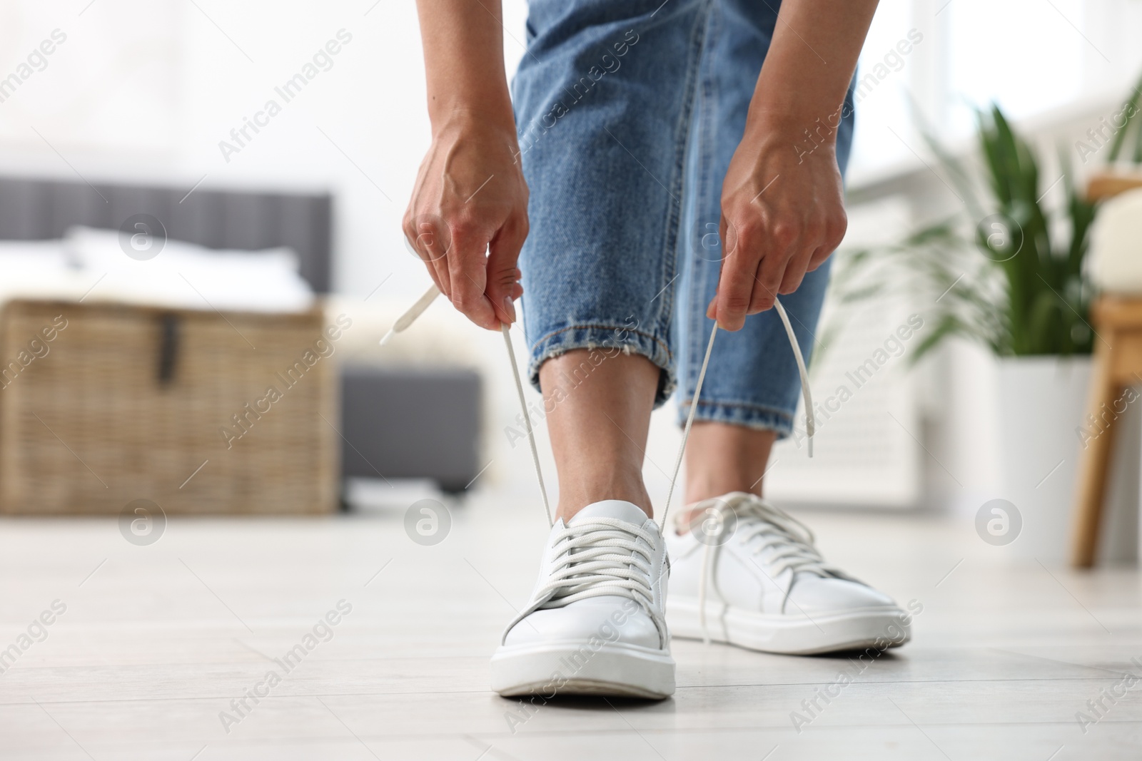 Photo of Woman tying shoelace of white sneaker indoors, closeup. Space for text