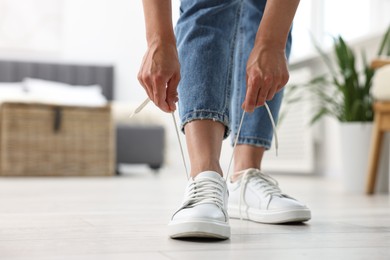 Photo of Woman tying shoelace of white sneaker indoors, closeup. Space for text