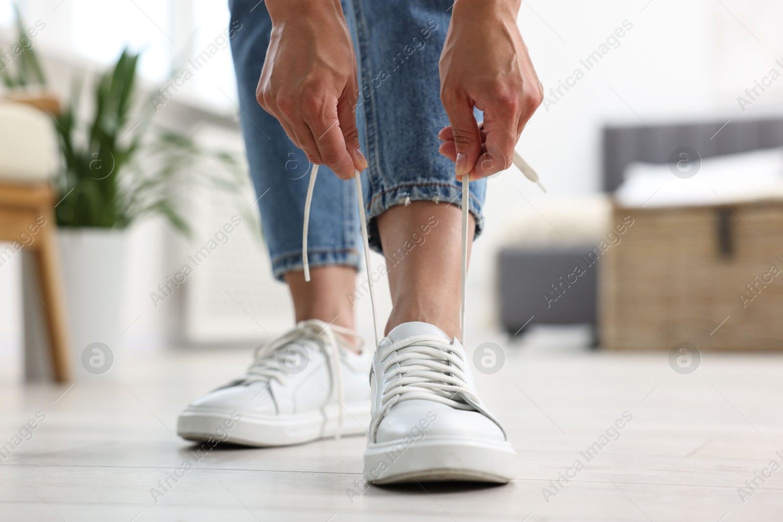 Photo of Woman tying shoelace of white sneaker indoors, closeup