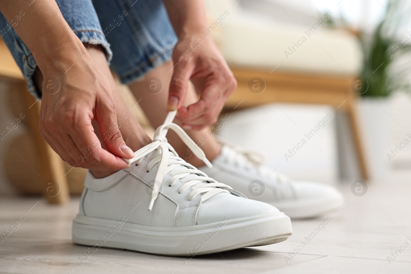 Photo of Woman tying shoelace of white sneaker indoors, closeup