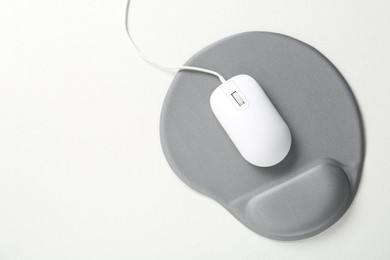 Photo of Computer mouse and mousepad with armrest on white table, top view. Space for text