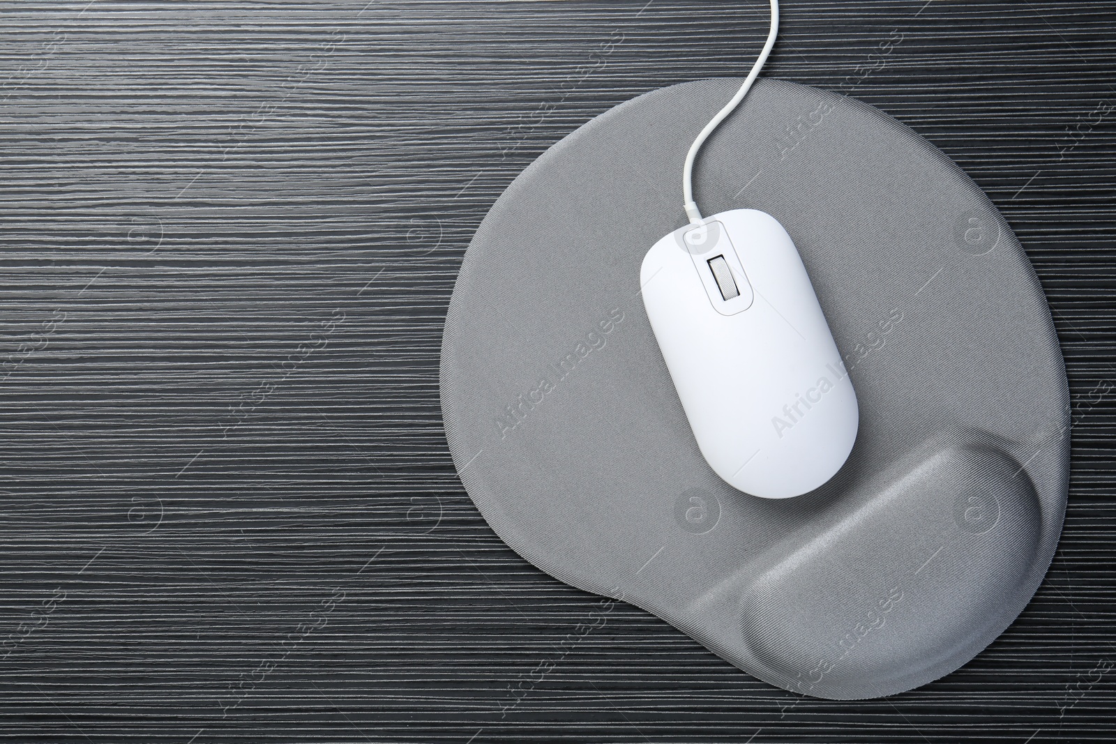 Photo of Computer mouse and mousepad with armrest on black wooden table, top view. Space for text