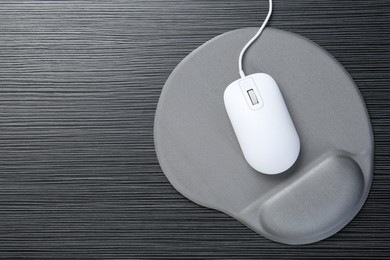 Photo of Computer mouse and mousepad with armrest on black wooden table, top view. Space for text