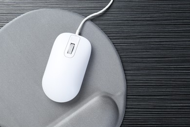 Photo of Computer mouse and mousepad with armrest on black wooden table, top view. Space for text