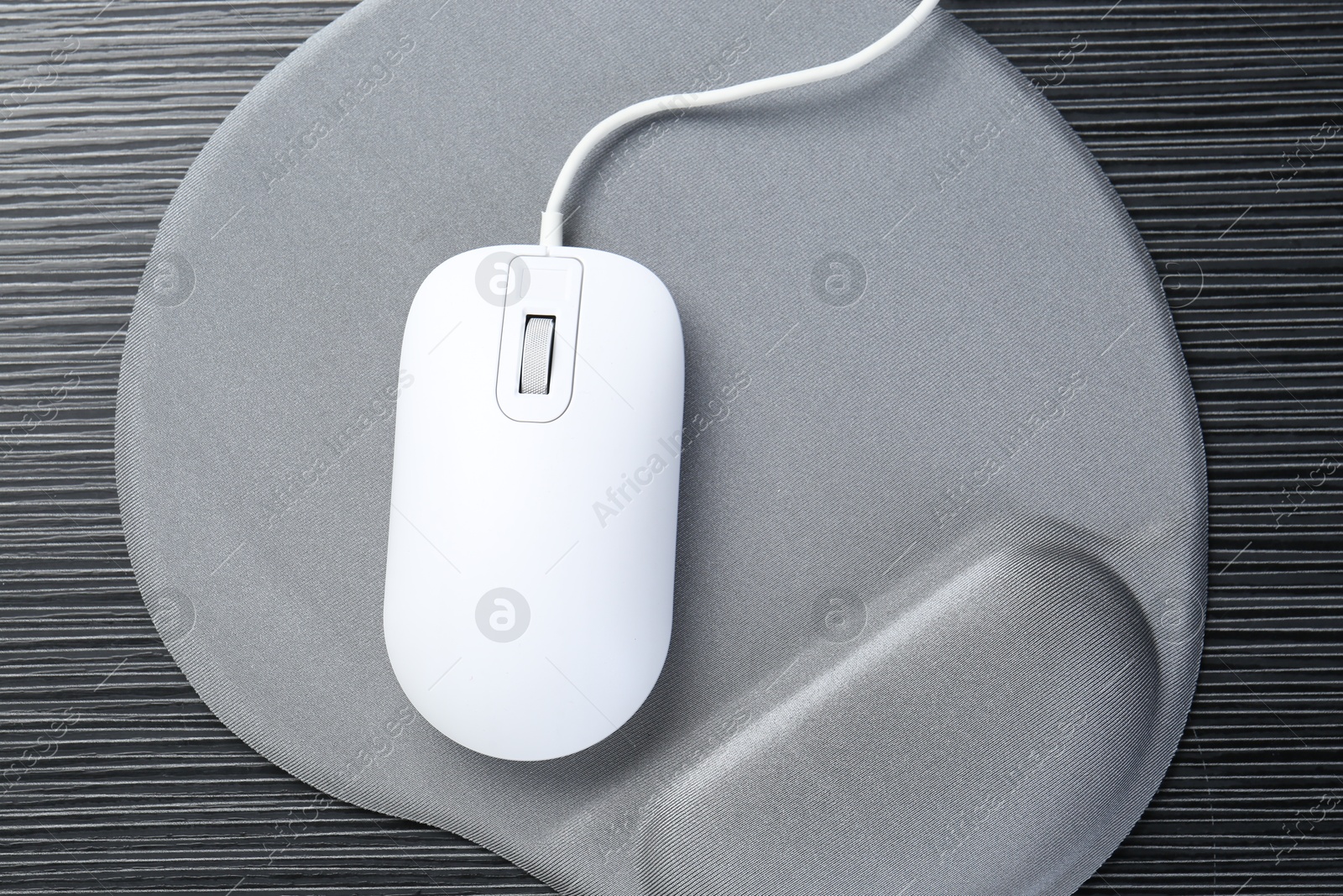 Photo of Computer mouse and mousepad with armrest on black wooden table, top view