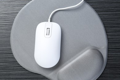 Photo of Computer mouse and mousepad with armrest on black wooden table, top view