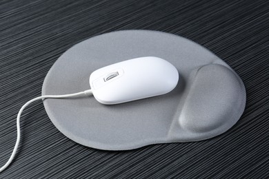 Photo of Computer mouse and mousepad with armrest on black wooden table