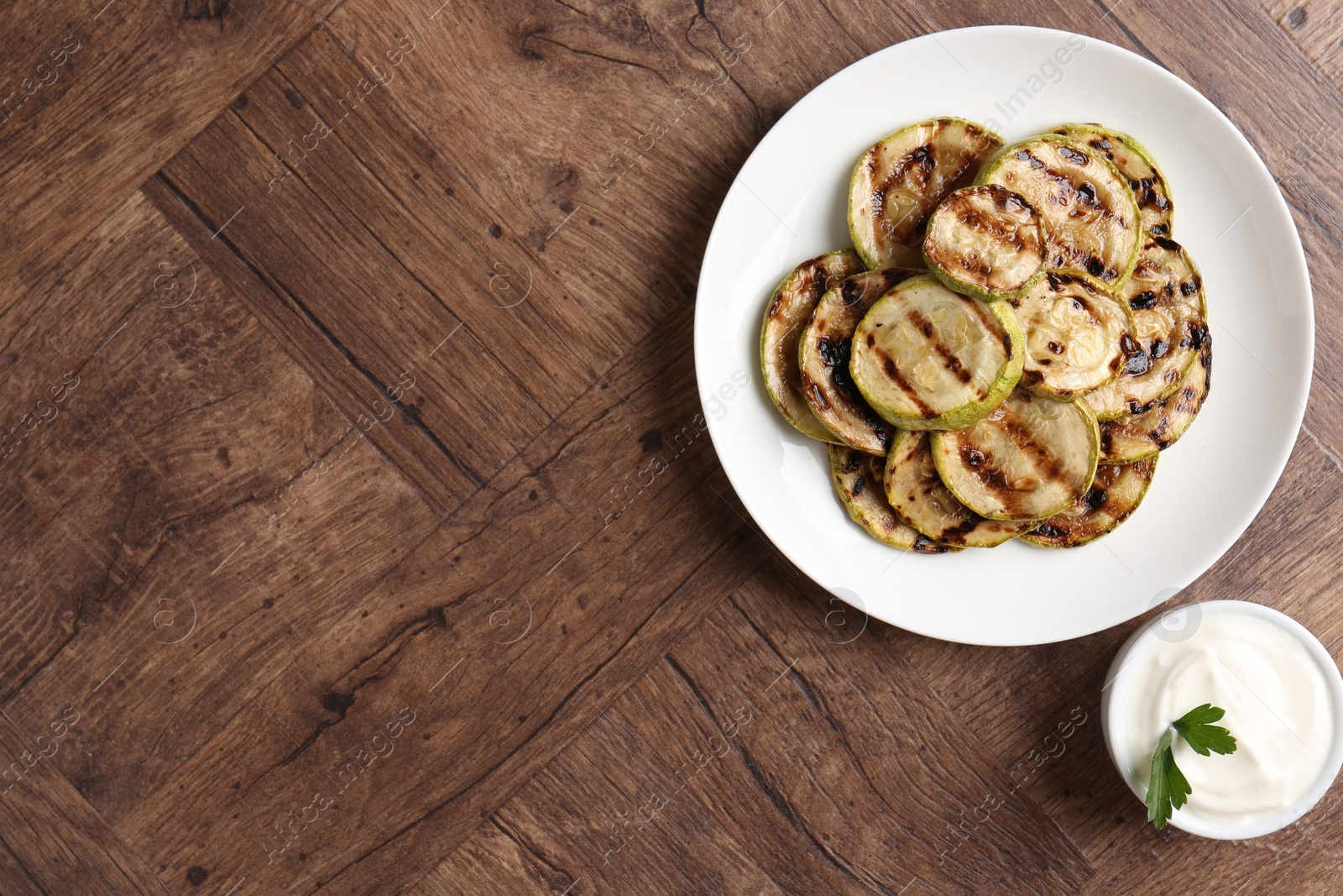 Photo of Tasty grilled courgette slices with sauce on wooden table, flat lay. Space for text