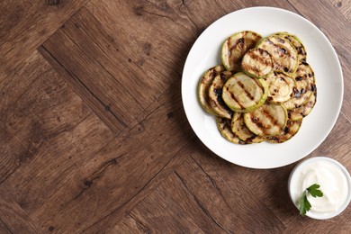 Photo of Tasty grilled courgette slices with sauce on wooden table, flat lay. Space for text