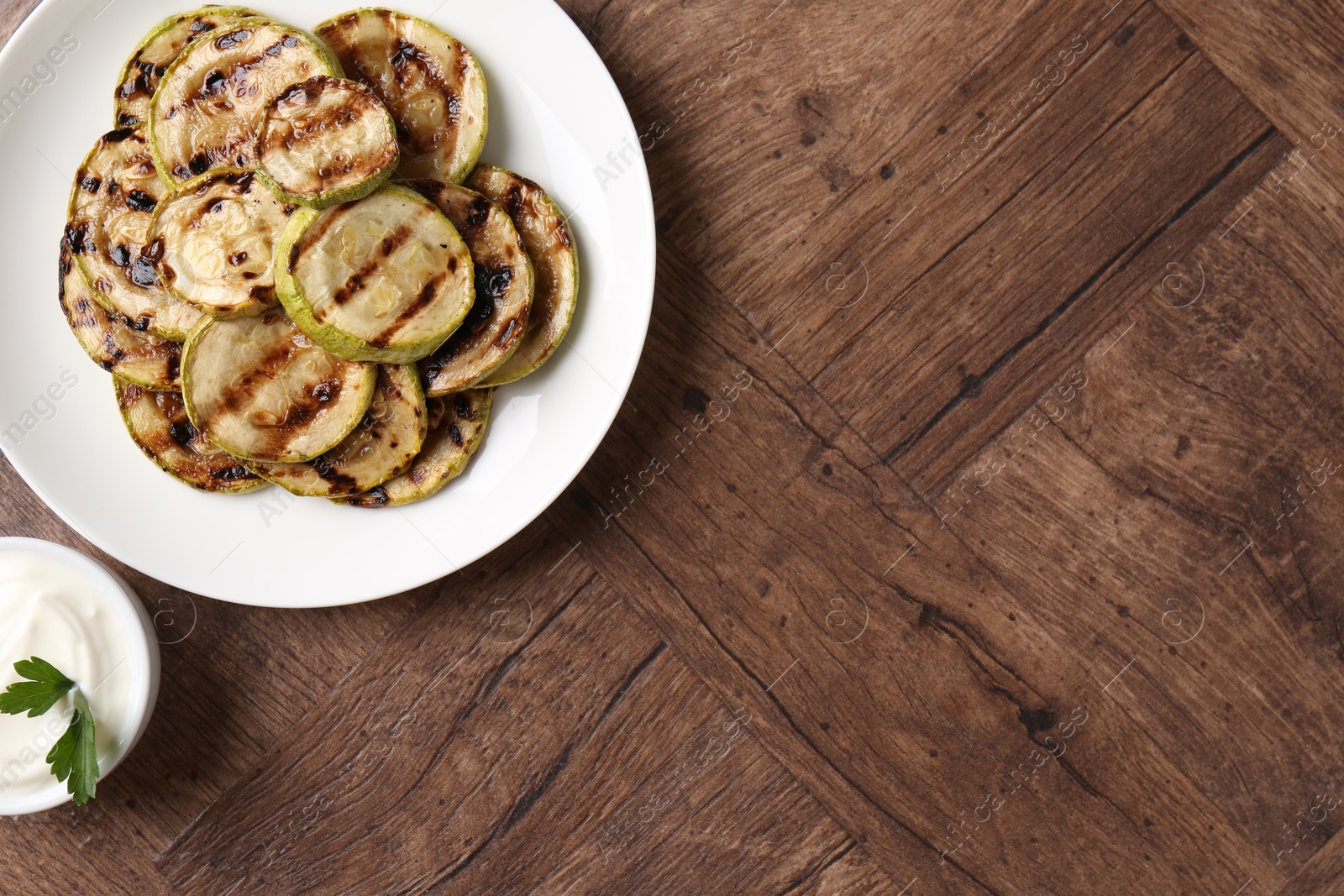 Photo of Tasty grilled courgette slices with sauce on wooden table, flat lay. Space for text