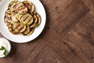 Photo of Tasty grilled courgette slices with sauce on wooden table, flat lay. Space for text