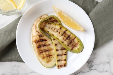 Tasty grilled courgette slices served on white marble table, flat lay