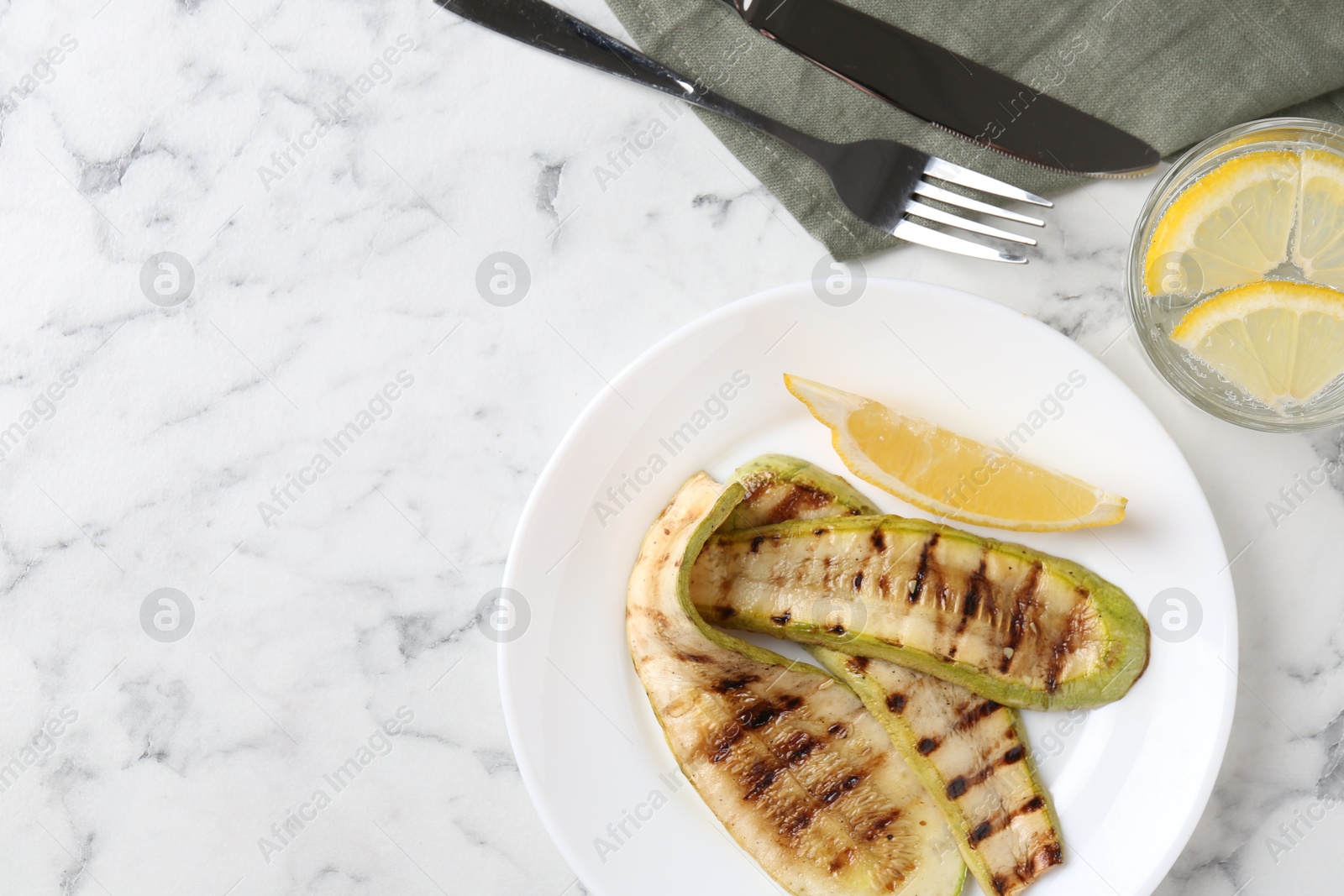 Photo of Tasty grilled courgette slices served on white marble table, flat lay. Space for text