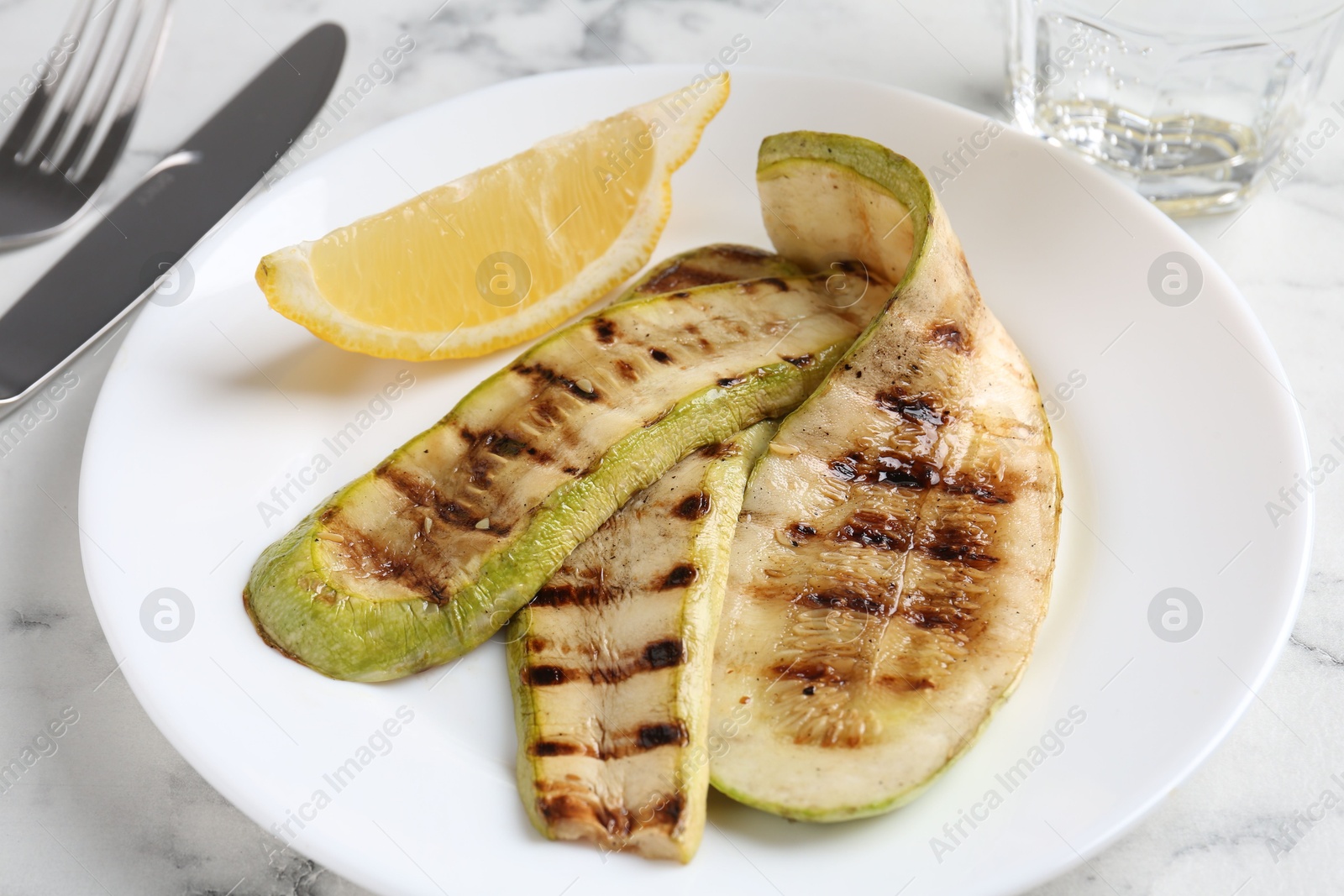 Photo of Tasty grilled courgette slices served on white marble table