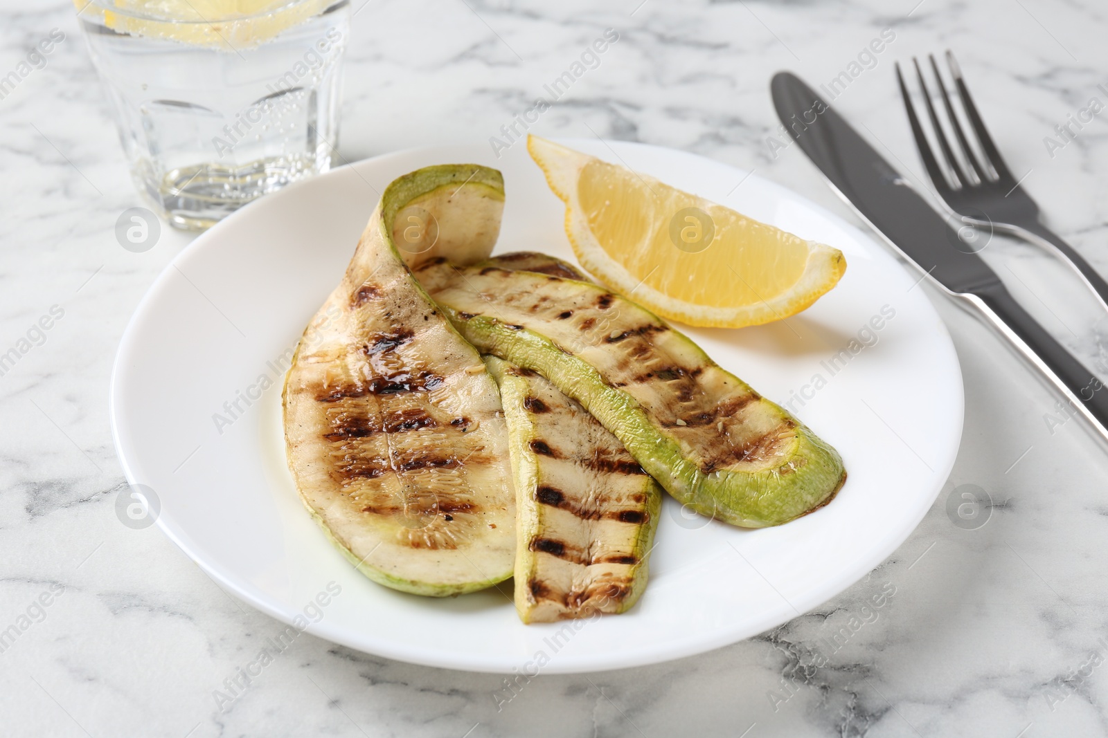 Photo of Tasty grilled courgette slices served on white marble table