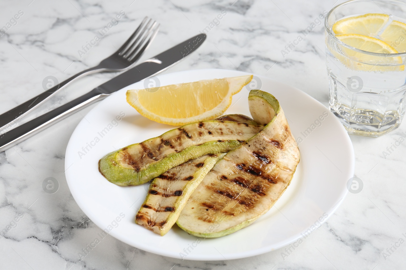 Photo of Tasty grilled courgette slices served on white marble table