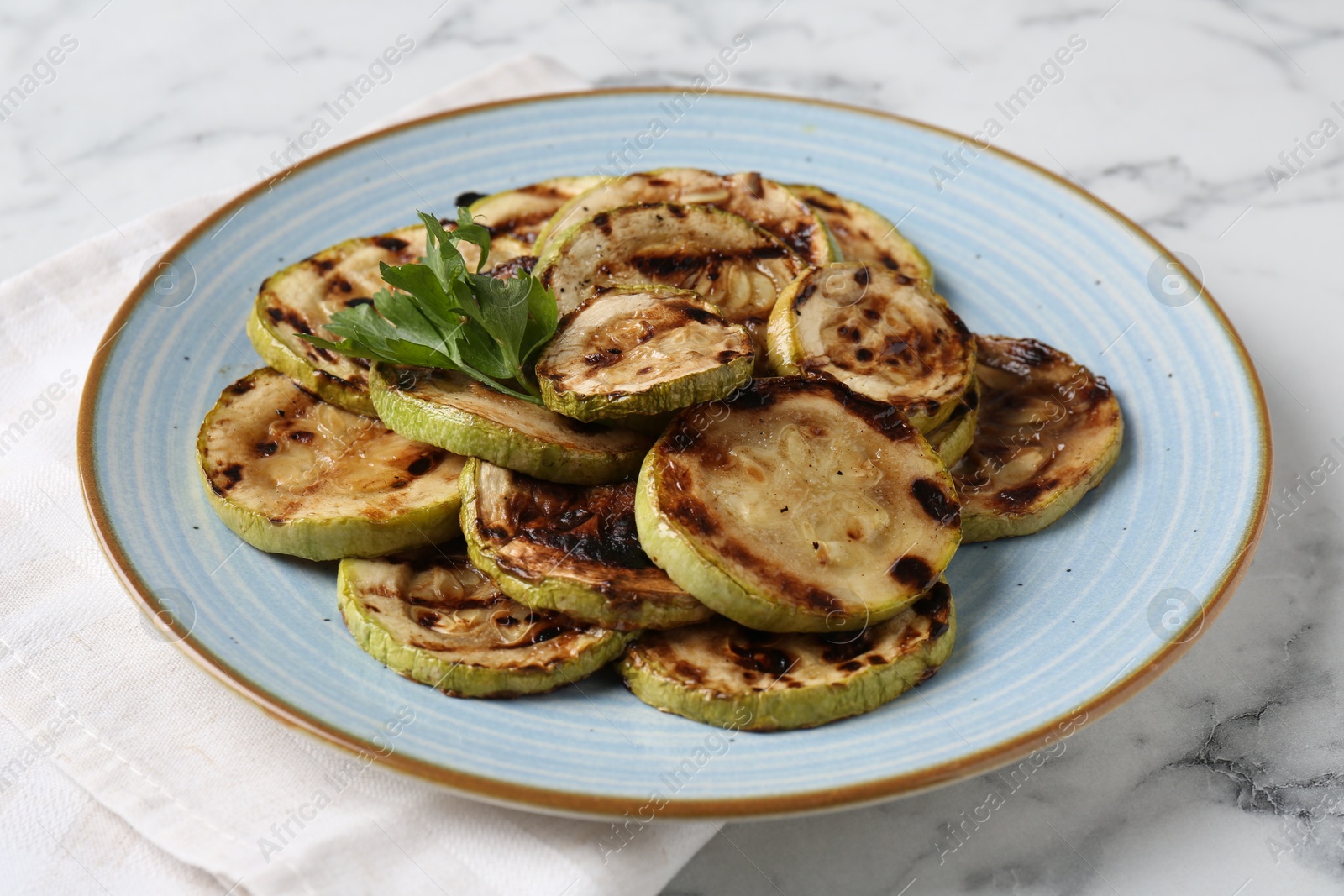 Photo of Tasty grilled courgette slices with parsley on white marble table