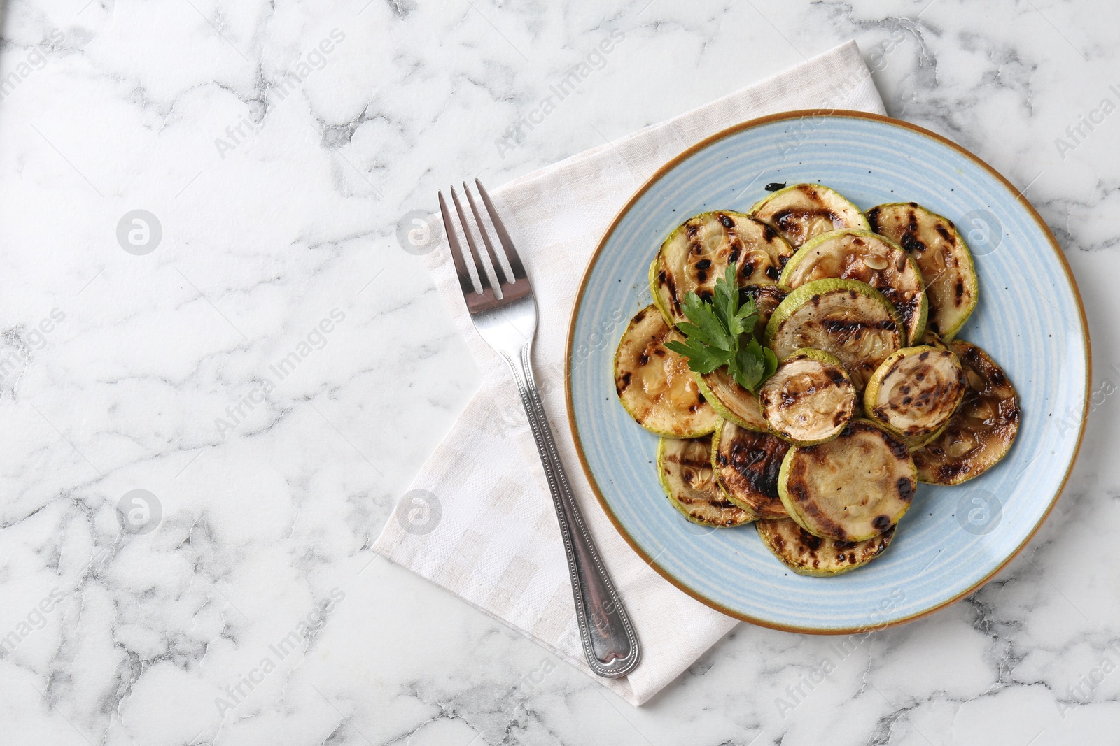 Photo of Tasty grilled courgette slices with parsley served on white marble table, flat lay. Space for text