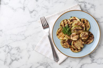 Photo of Tasty grilled courgette slices with parsley served on white marble table, flat lay. Space for text