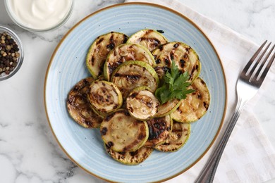 Photo of Tasty grilled courgette slices with parsley served on white marble table, flat lay