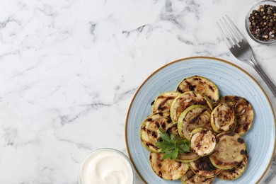 Tasty grilled courgette slices served on white marble table, flat lay. Space for text