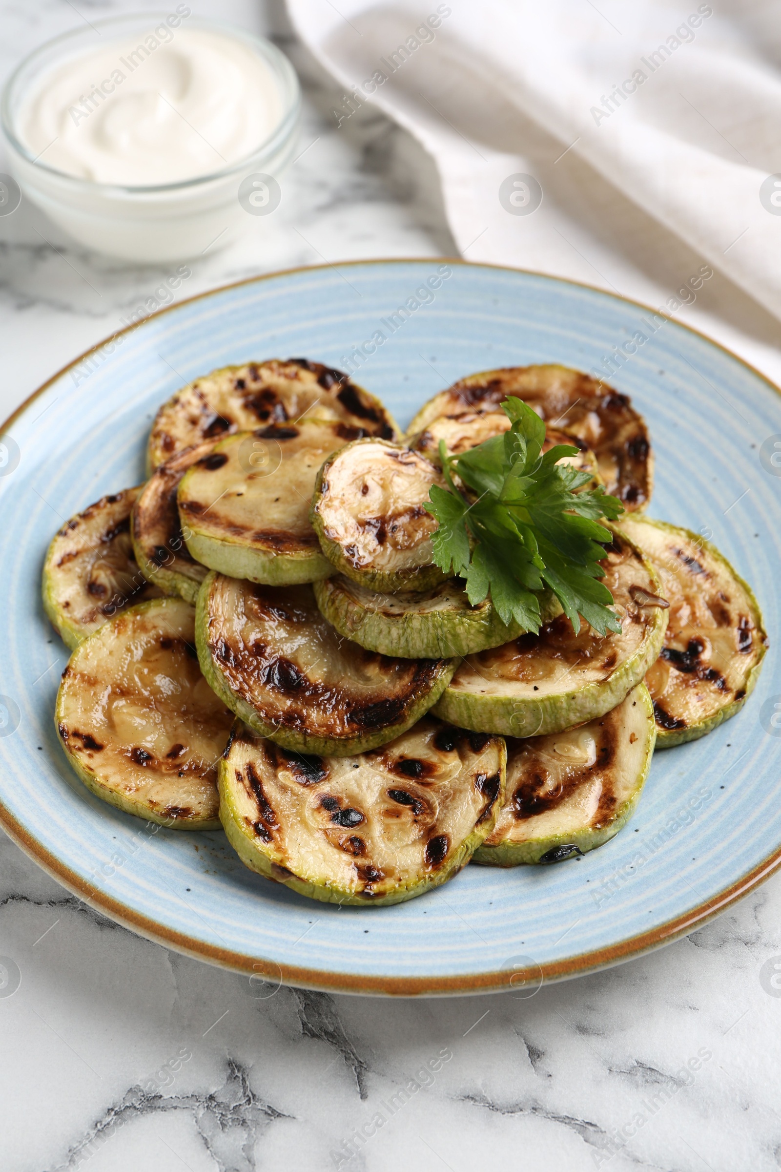 Photo of Tasty grilled zucchini slices with parsley on white marble table