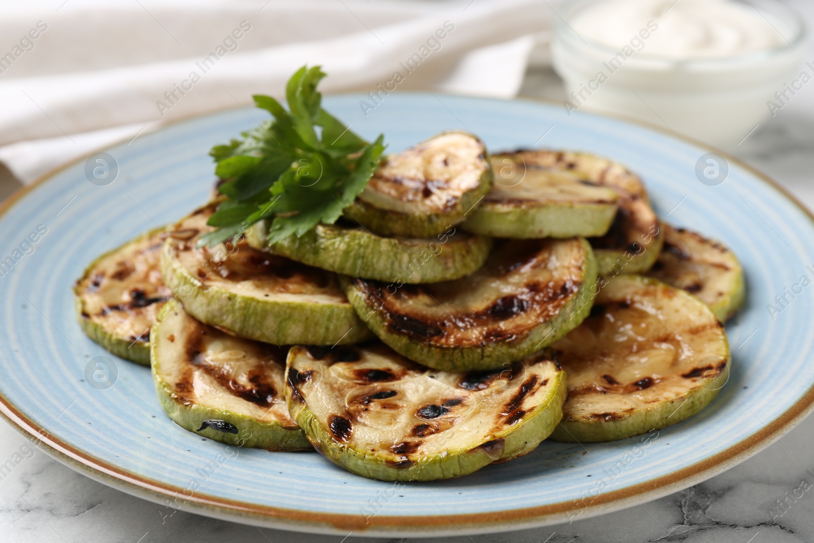 Photo of Tasty grilled zucchini slices with parsley on white marble table, closeup