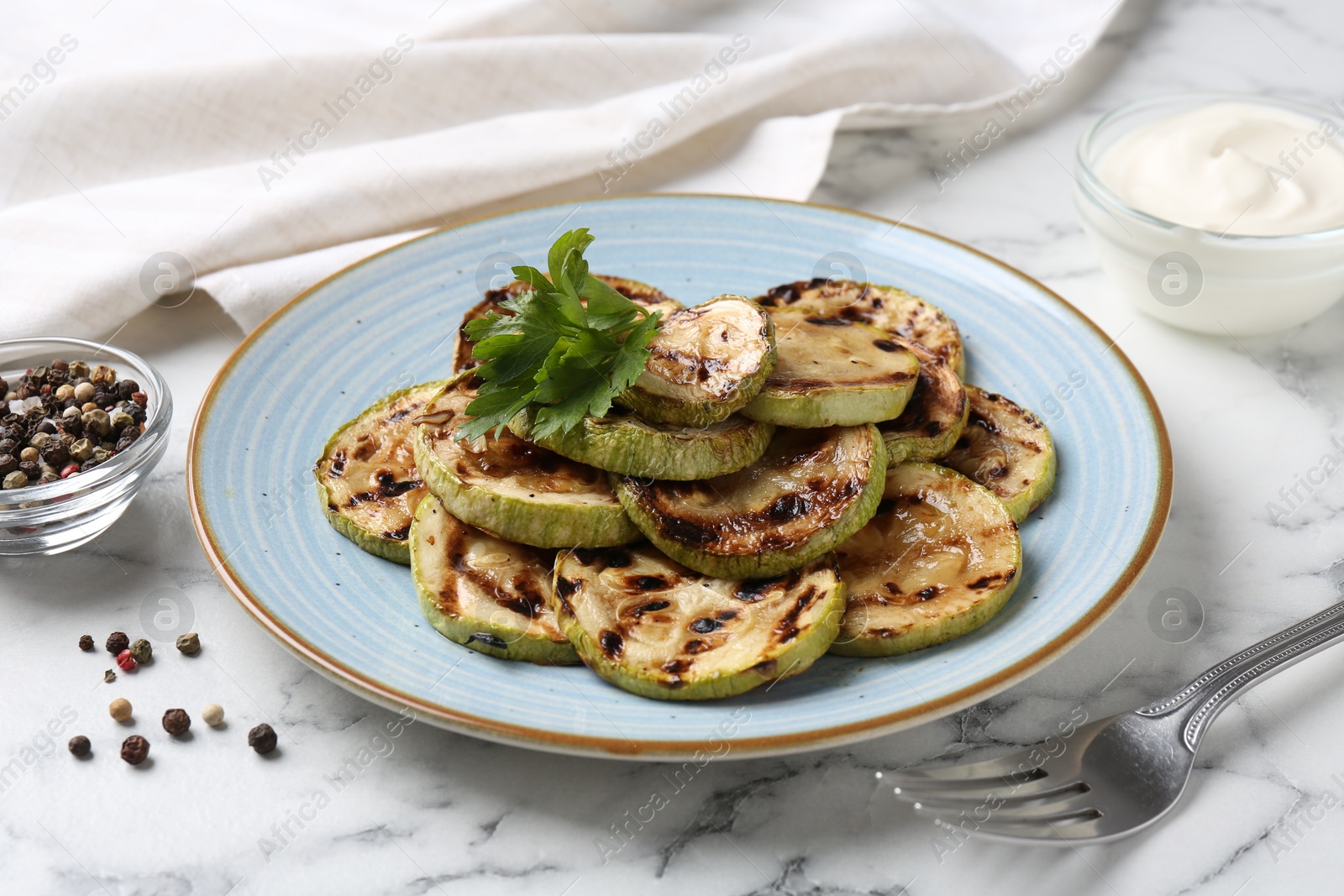 Photo of Tasty grilled zucchini slices with parsley served on white marble table