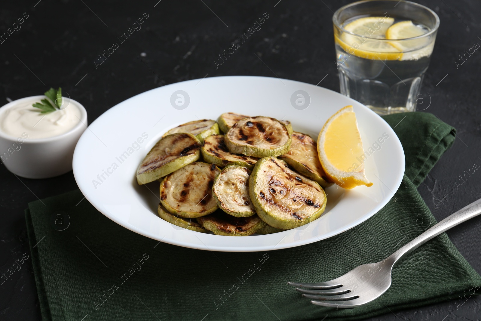 Photo of Tasty grilled zucchini slices served on black table