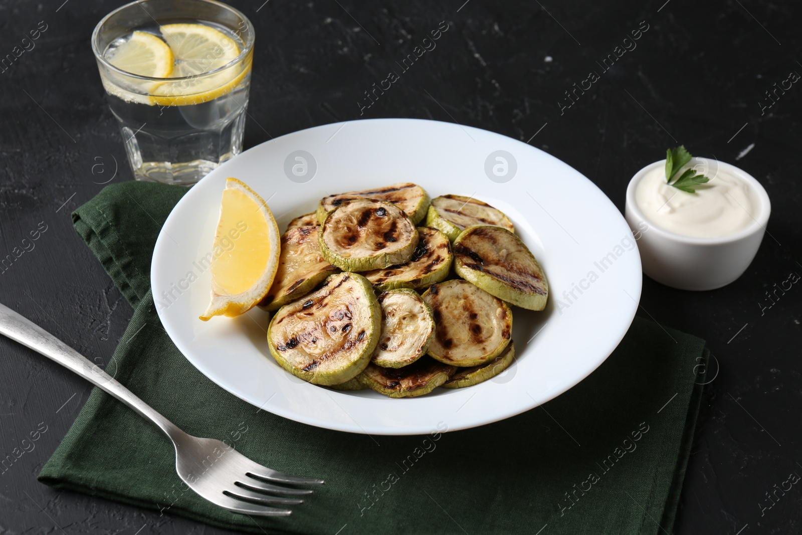 Photo of Tasty grilled zucchini slices served on black table