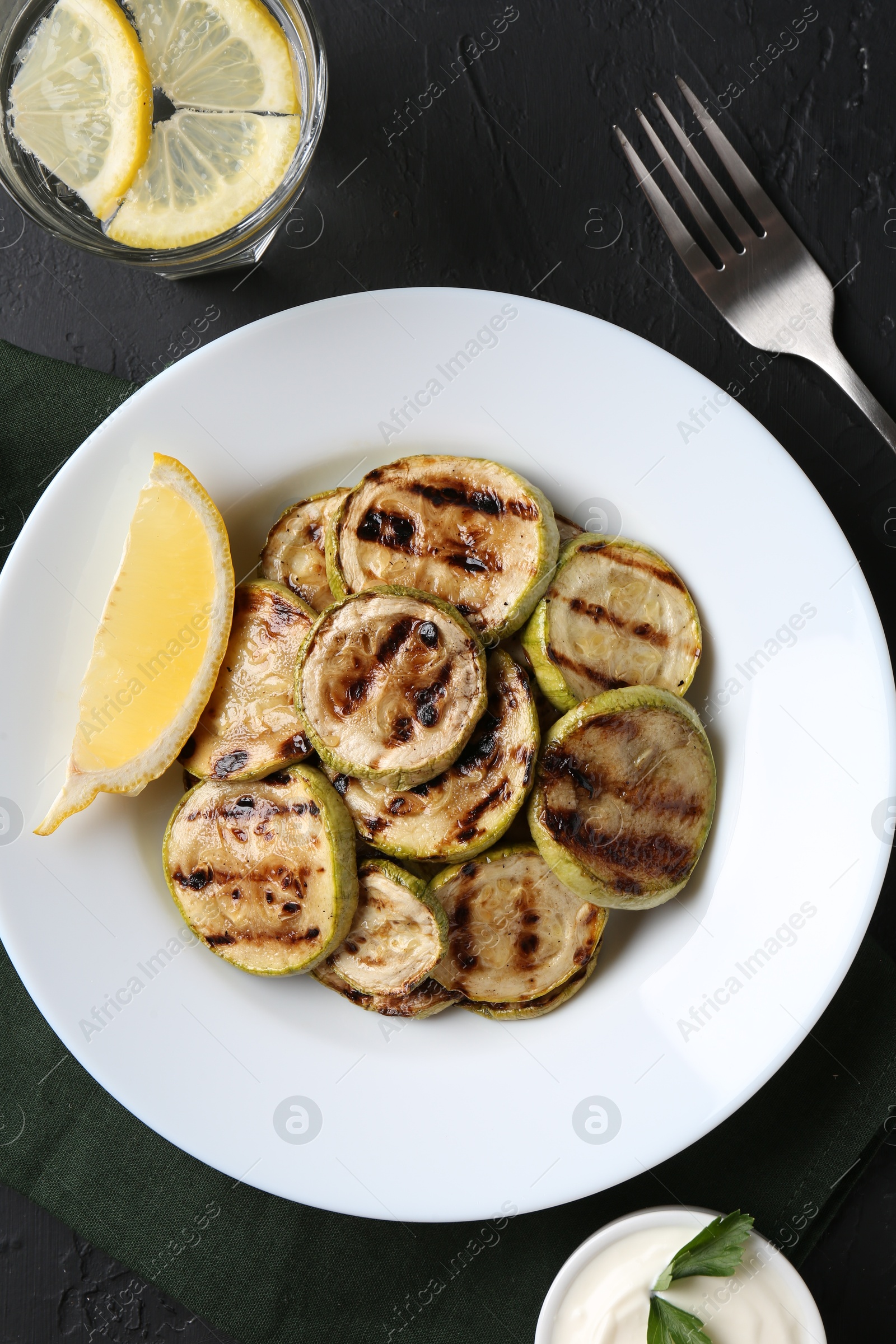 Photo of Tasty grilled zucchini slices served on black textured table, flat lay