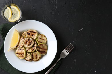 Photo of Tasty grilled zucchini slices served on black textured table, flat lay. Space for text