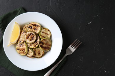 Photo of Tasty grilled zucchini slices served on black textured table, flat lay. Space for text