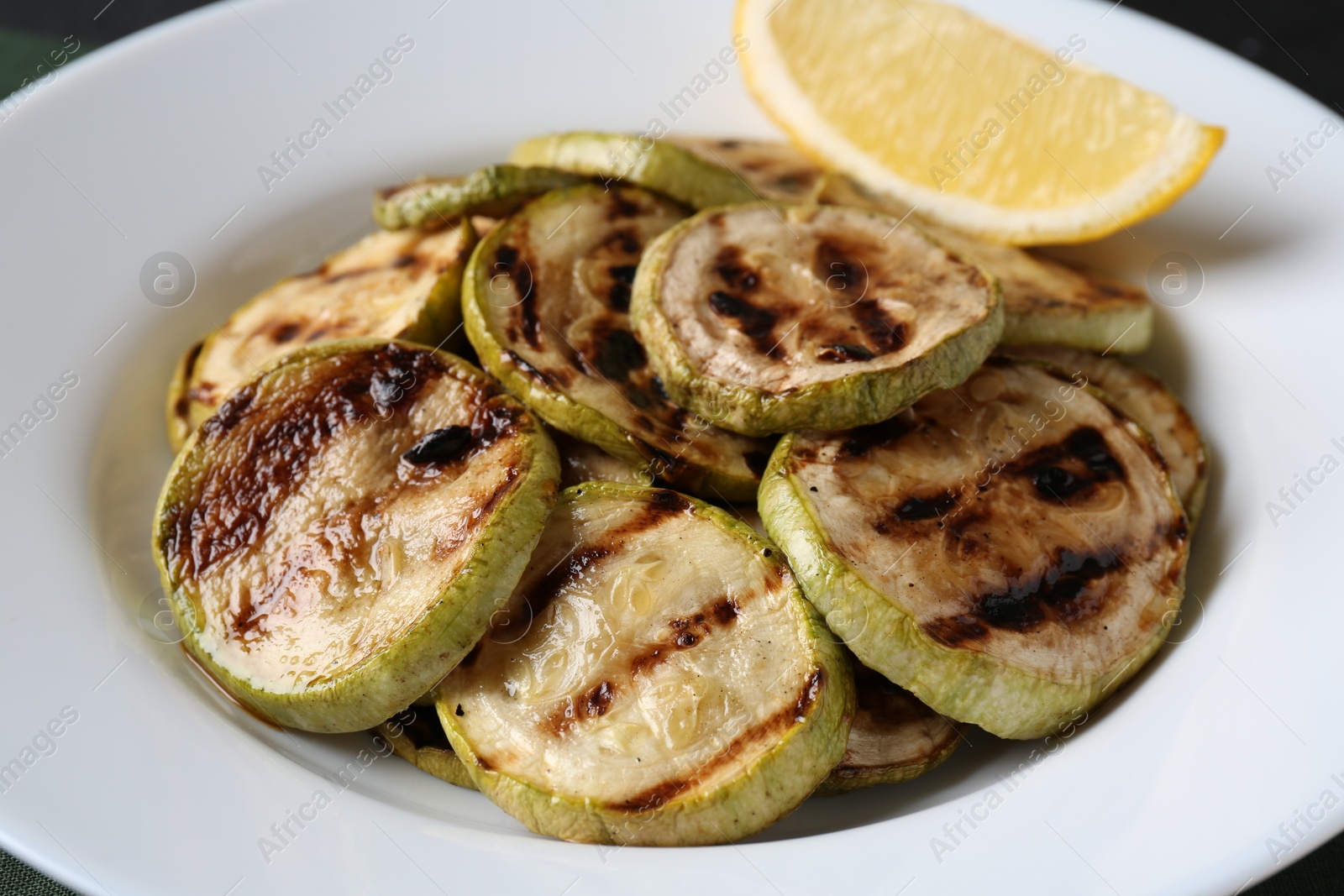 Photo of Tasty grilled zucchini slices with lemon on black table, closeup