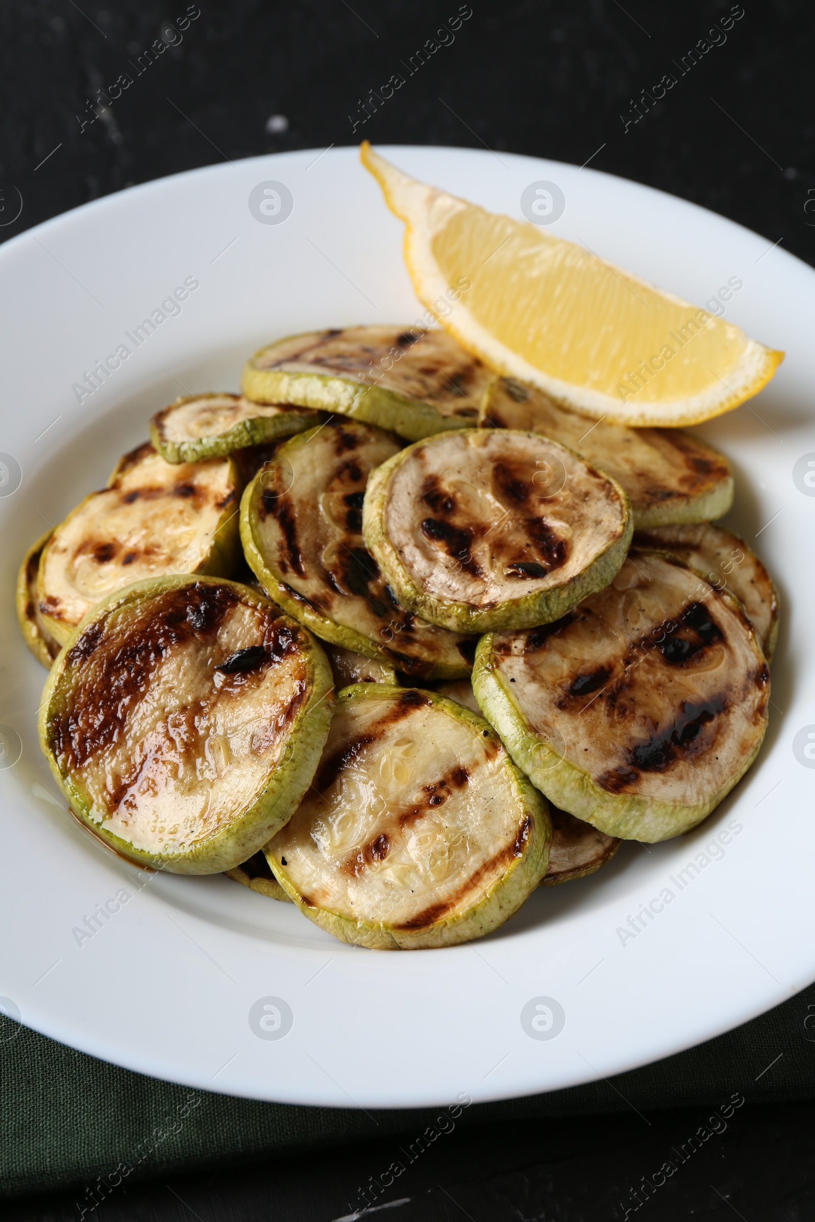 Photo of Tasty grilled zucchini slices with lemon on black table