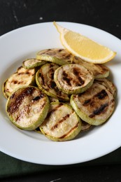 Photo of Tasty grilled zucchini slices with lemon on black table