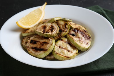 Photo of Tasty grilled zucchini slices with lemon on black table