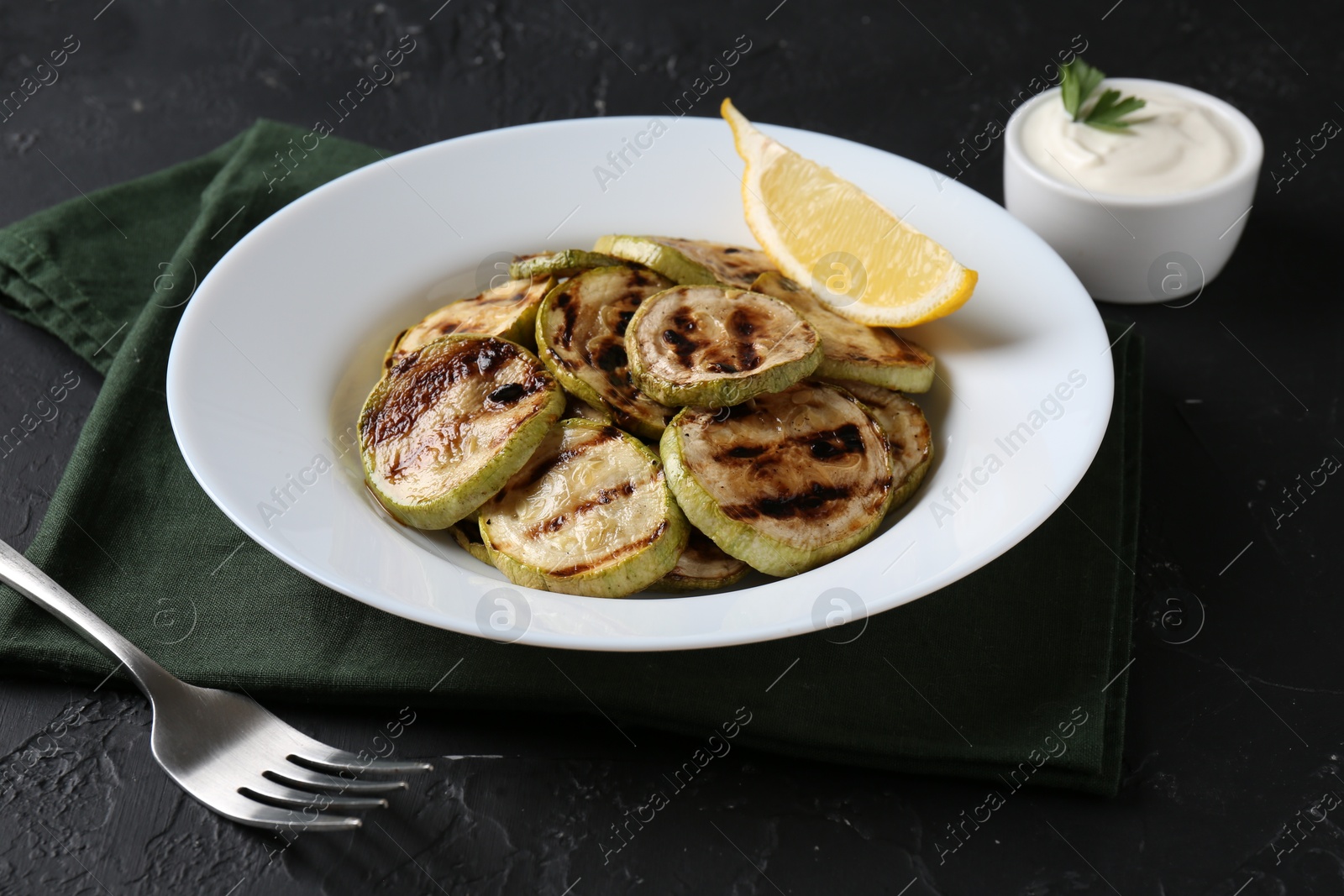 Photo of Tasty grilled zucchini slices served on black textured table