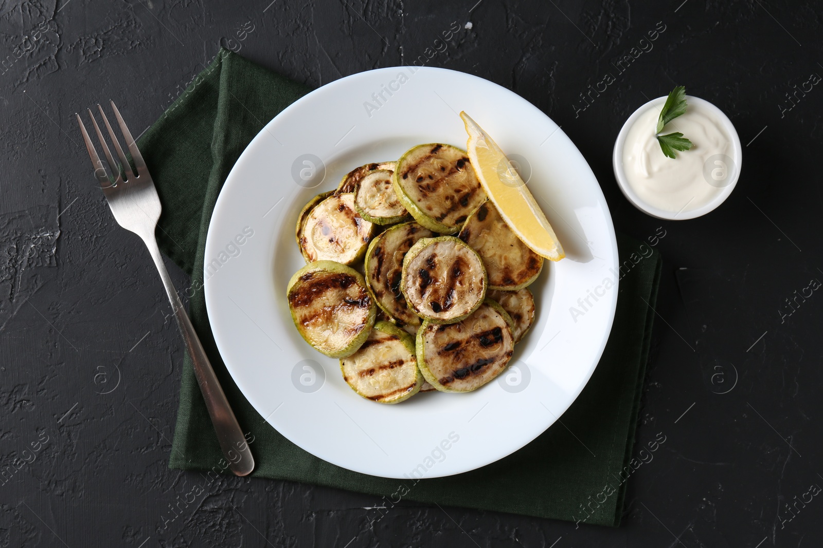 Photo of Tasty grilled zucchini slices served on black textured table, flat lay